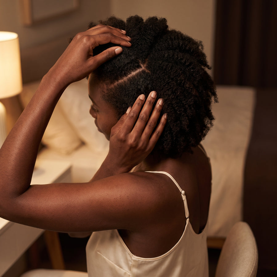 Parting textured hair at a bedroom vanity to expose the scalp