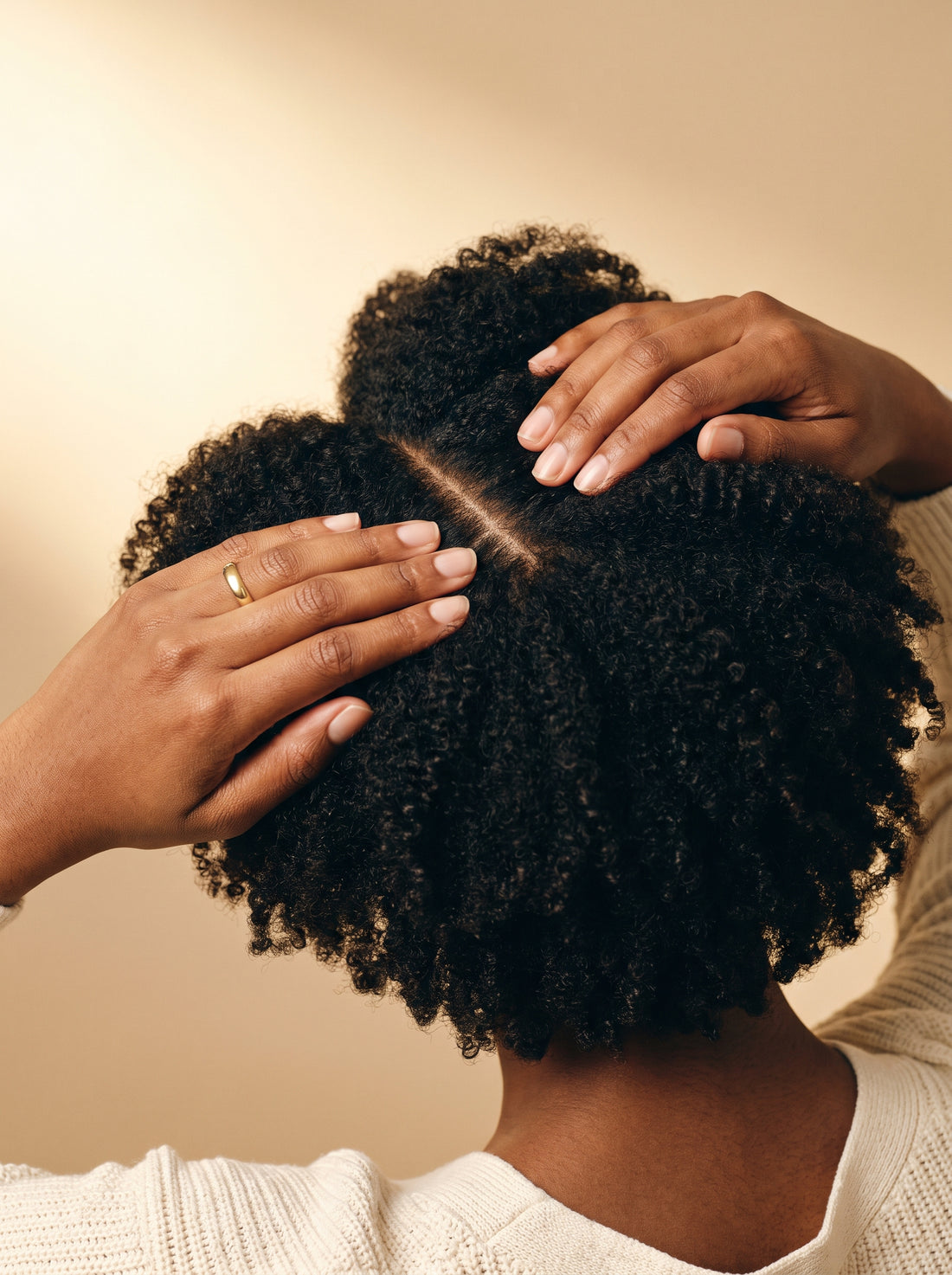 A woman parting her natural coils at the crown to reveal a healthy scalp