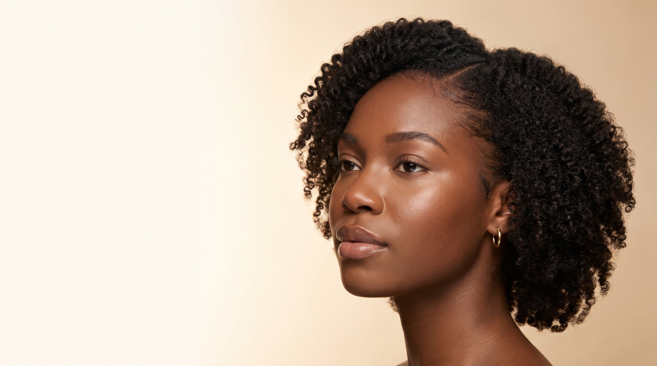 A young Black woman in profile against a cream backdrop, her natural coils neatly parted at the crown